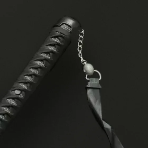 Gros plan sur l'édition Shadow : poignée tressée noire, chaînette et ruban